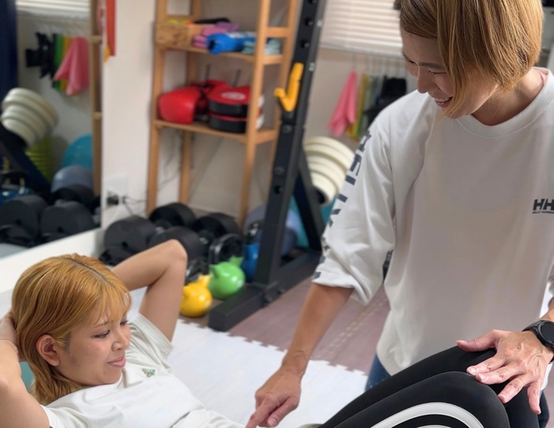 トレーナーのサポートで体幹のエクササイズを行う女性
